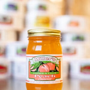 A jar of peach jam sitting on top of a counter.