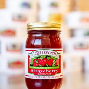 A jar of strawberry preserves on top of a table.