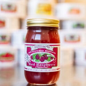 A jar of red raspberry jam on top of a table.