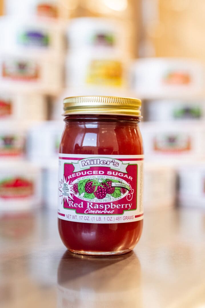 A jar of red raspberry jam on top of a table.