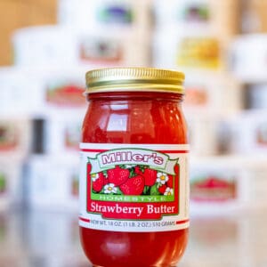 A jar of strawberry butter sitting on top of a table.